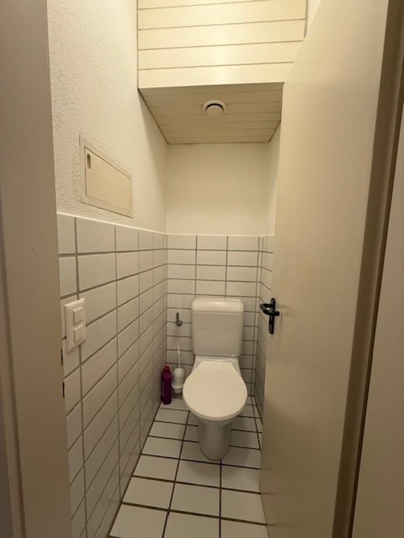 small bathroom with white tiles, toilet, and a small shelf