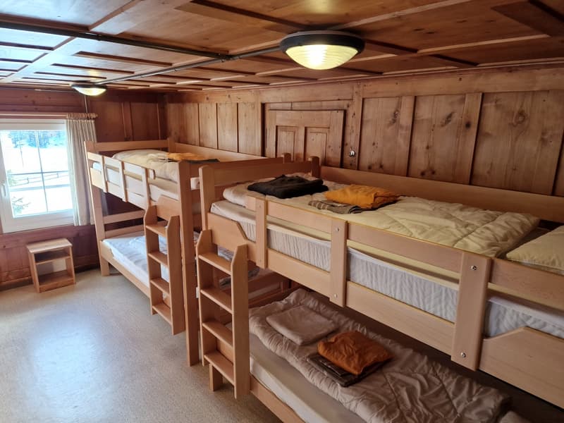 4 stacked wooden bunk beds, small wooden bedside table, large windows with curtains