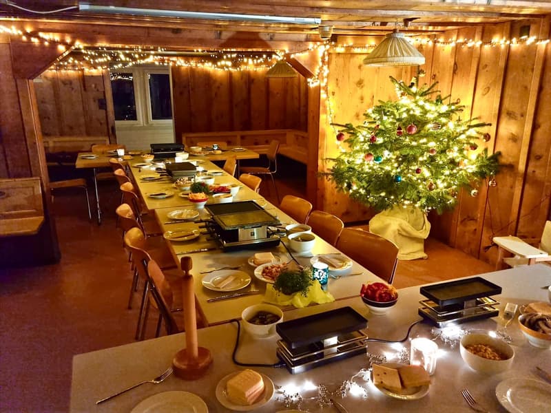 long dining table with various food for Christmas party, lit up Christmas tree, wooden benches, wooden ceiling