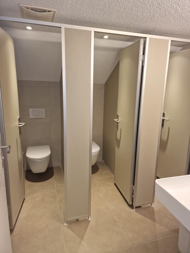 Bathroom, two white toilet cubicles, white wall tiles, tiled floor, white sink, three grey doors