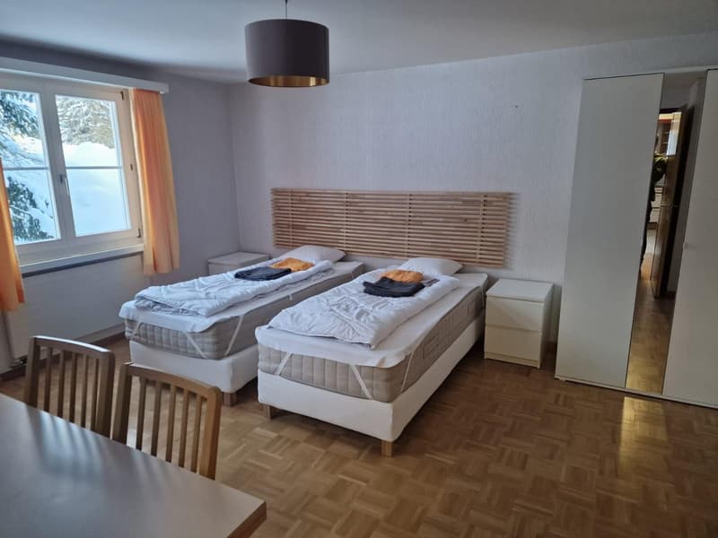 bedroom with two single beds, two night stands, wooden bed head, lamp, white walls, window, curtains, chairs, desk