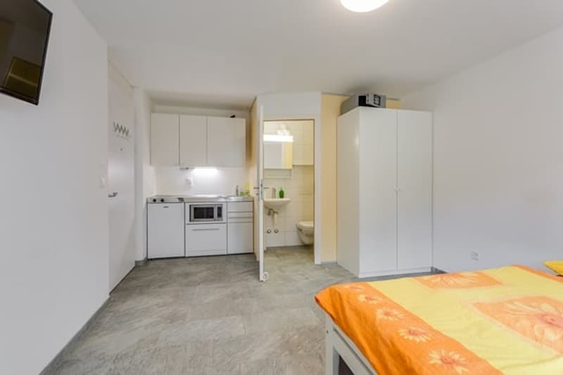small room with bed, kitchen, sink, microwave, refrigerator, toilet, cabinets, television