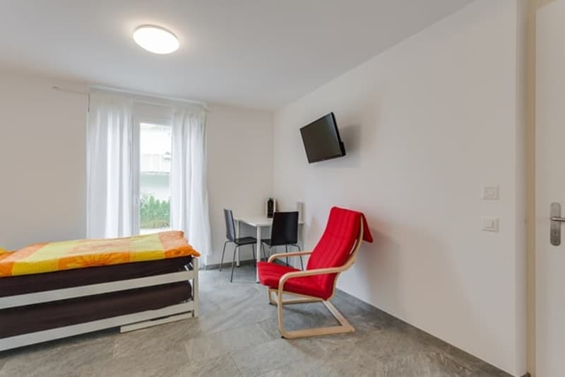 small room with bed, chair, desk, TV, window