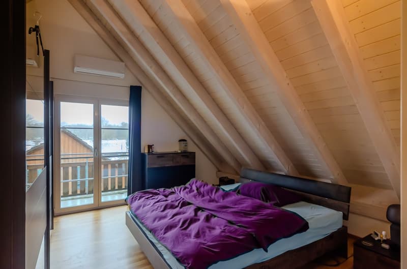 wooden ceiling, wooden floor, double bed with purple blanket, balcony, wooden dresser, glass doors, window