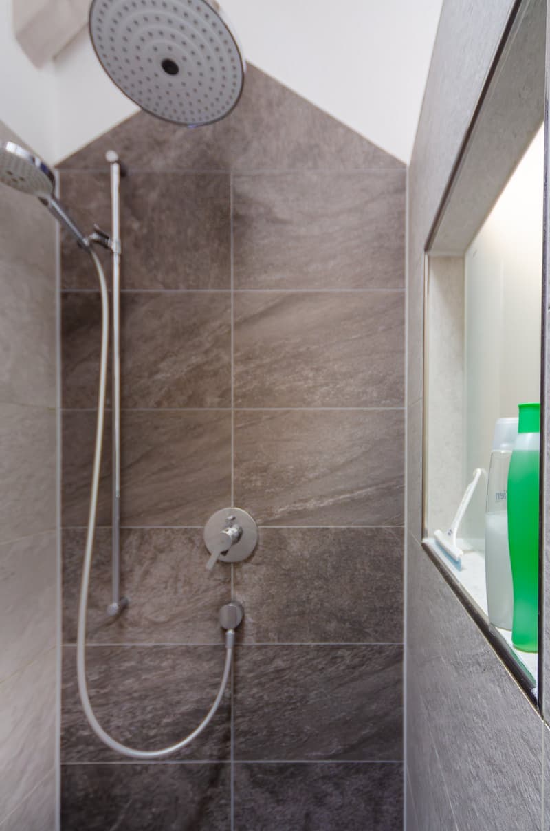 shower area with tiled walls, showerhead, shower hose, mirror with soap holders