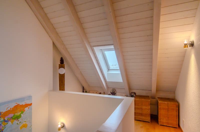 angled attic room with white walls, wooden beams, skylight, a world map, and a wooden chest