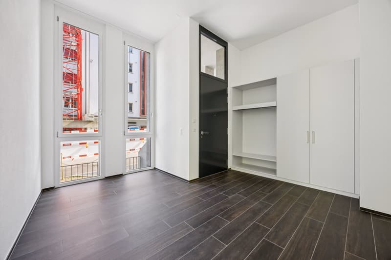 Modern room, with large windows, dark wood floor, tall white cabinets, doors
