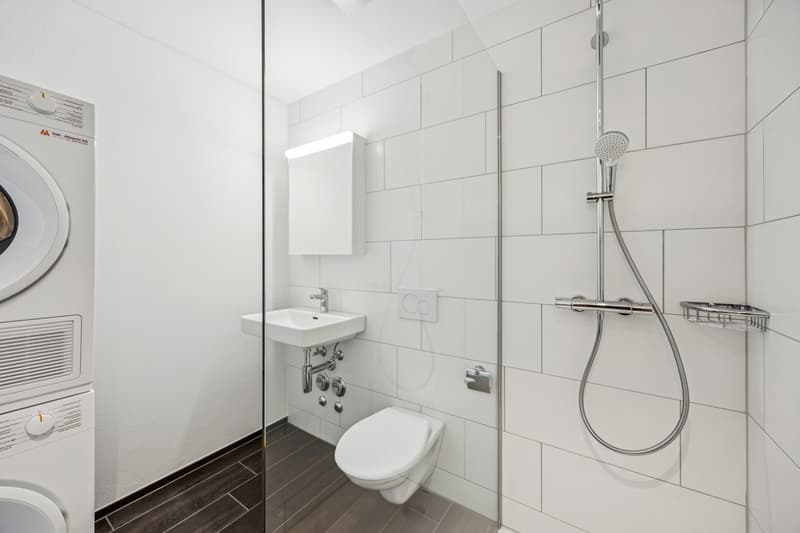 modern bathroom with white tiles, shower, sink, toilet, and washing machine