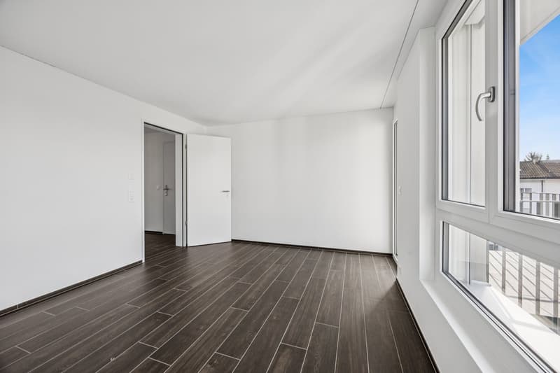 Empty room with wooden floor, white walls, and large windows that lead to a balcony with a railing