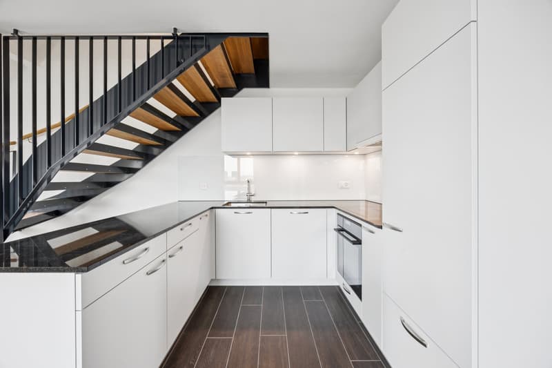 modern kitchen, black counter, wooden stairs, white cabinets, sink, black and brown floors