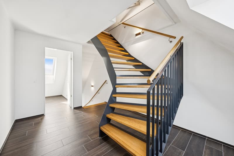 White walls, wooden stairs, dark floor, handrails