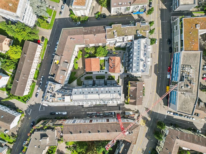 Aerial view of apartment buildings with various colors and designs, a red crane in the center, road, street and trees in the area.