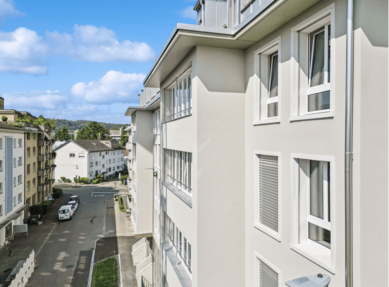 Modern white apartment building, multiple windows, white exterior, flat rooftop, multiple parking spots