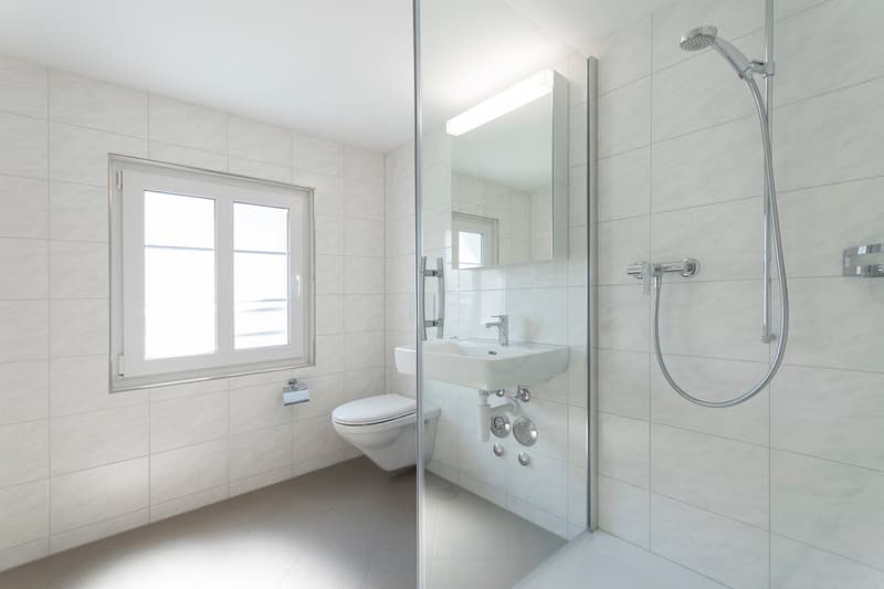 modern bathroom, white tiles, glass shower, sink, toilet, natural light from window