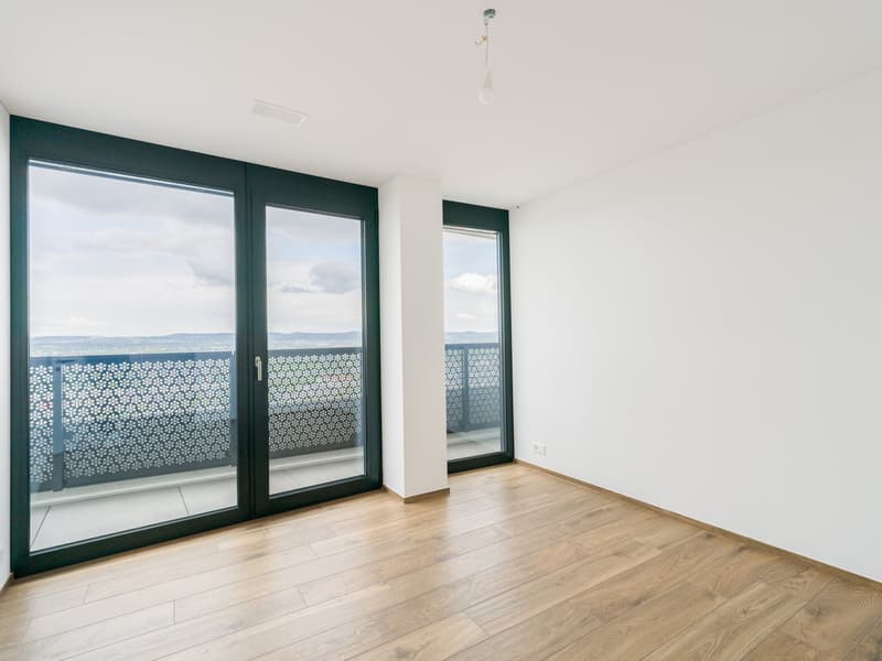 wooden floor, large sliding glass doors leading to a balcony, white walls, modern ceiling light, balcony with black railing