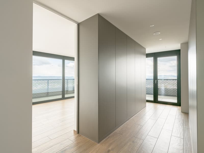 Empty room with wooden floor, large windows, balcony with railing, sliding doors, built-in wardrobe