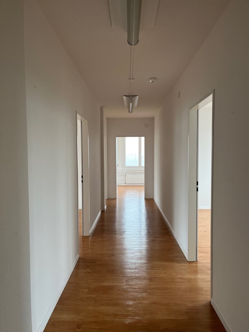 Empty hallway with wooden floors, white walls, and ceiling lights