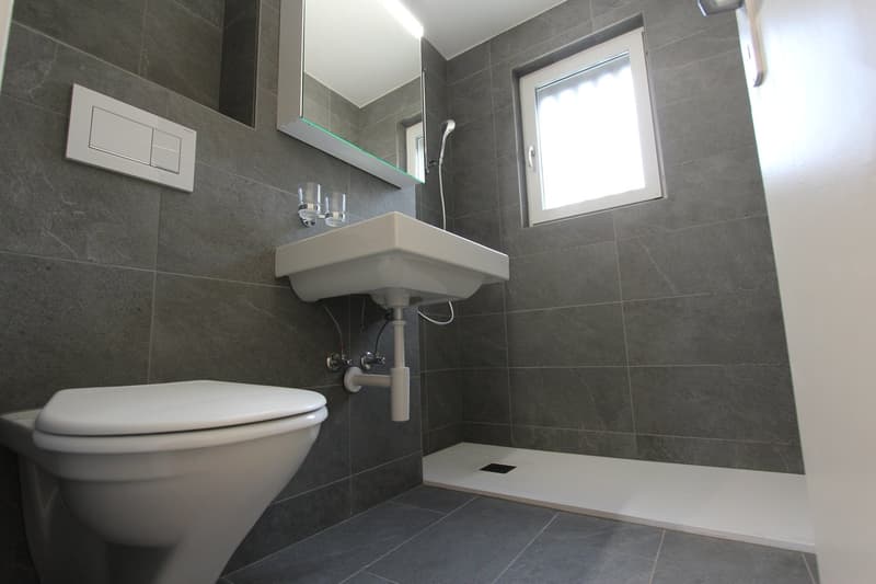 modern bathroom with gray tiles, white toilet, white sink, mirror, window, shower area