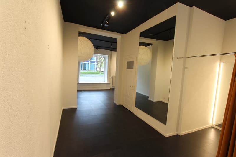Empty hallway with white walls, black floor, two large mirrors, and a window.