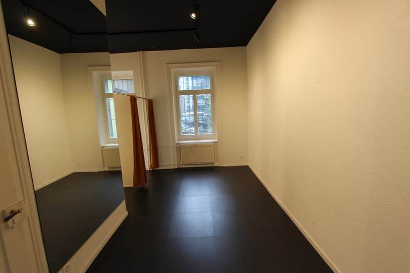 Empty room with black floor, white walls, two windows, radiators, and a mirror.