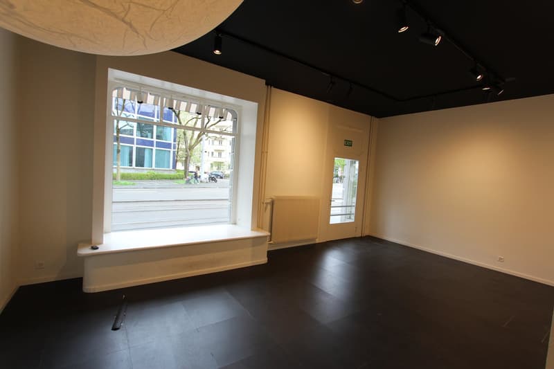 Empty room with large window, radiator, black floor, white walls, window seat, exit sign
