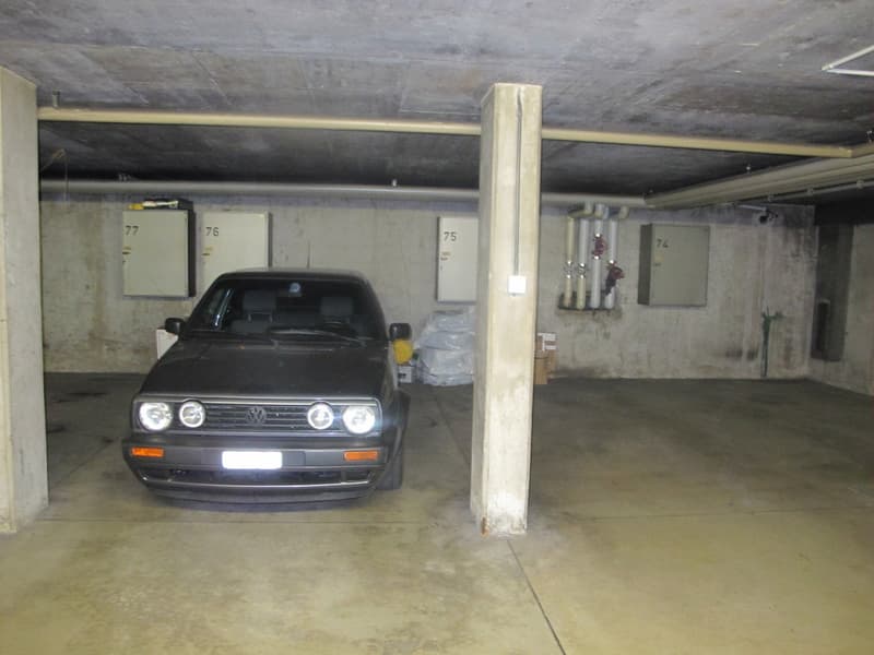 underground parking space with concrete walls, pillar, ceiling with beams, electrical boxes, one car parked