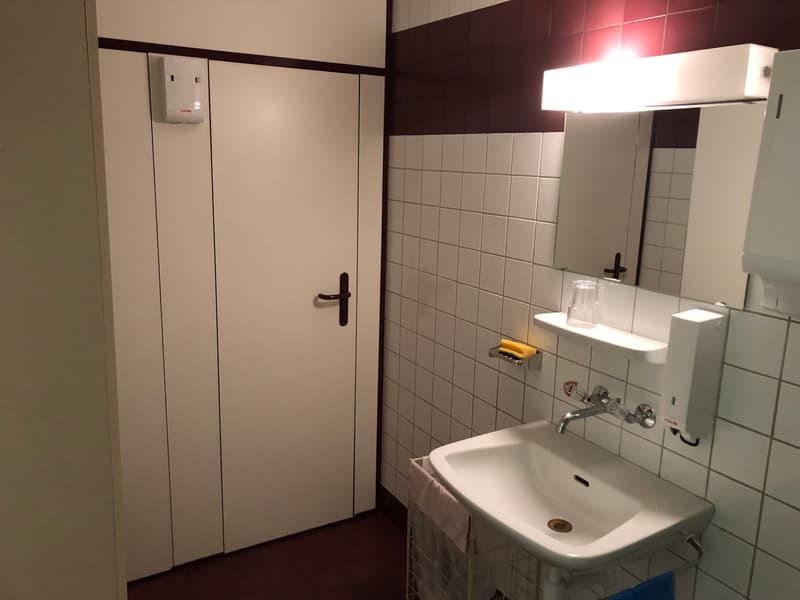 Tiled bathroom with a white sink, mirror, and a white door leading to another room. The bathroom appears to have a private washing machine installed.