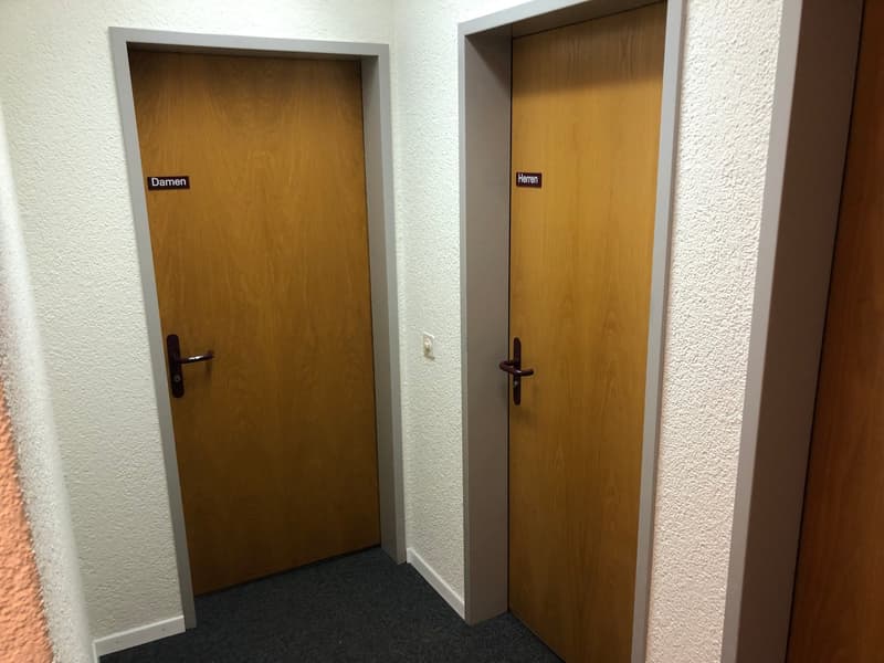 The image shows two wooden doors labeled 'Damen' (Ladies) and 'Herren' (Gentlemen), indicating this is a restroom area with separate entrances for men and women.