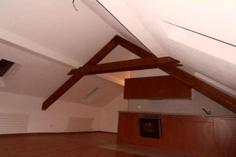 empty attic room with wooden beams, kitchen area with oven, wooden cabinets, and a sink