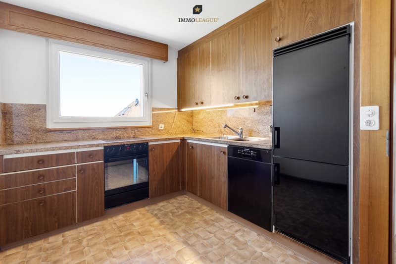 Küche mit Charakter: warme Holzfronten treffen auf moderne Einbaugeräte, dazu ein grosses Fenster mit Ausblick.
