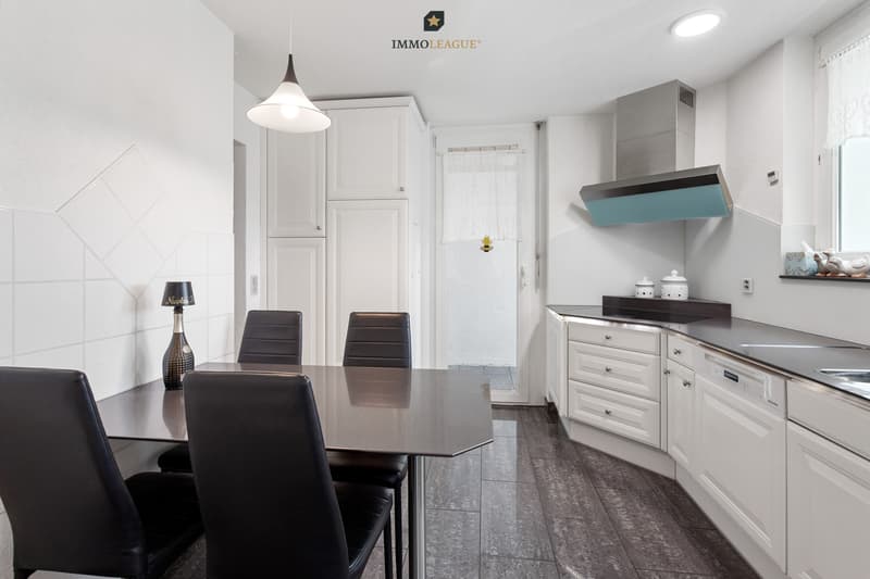 Charmante, helle Küche im Landhausstil mit Vollflächeninduktionskochfeld, Steamer und Backofen. Das angrenzende Reduit bietet wertvollen Stauraum.