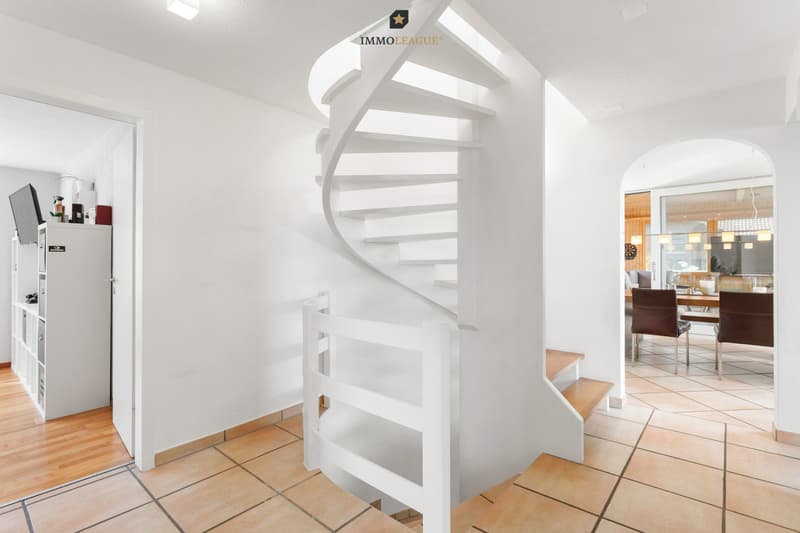 Die geschwungene Wendeltreppe verbindet die Geschosse mit eleganter Linienführung und nimmt die runde Form des Durchgangs zum Essbereich auf.