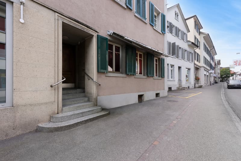 Facade of building with green shutters, steps leading to the door, beige concrete walls, no visible features