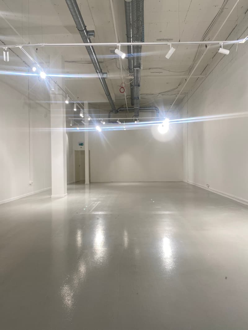 The image shows a large, open commercial space with a high ceiling, exposed ductwork, and bright lighting. The space appears to be a warehouse, office, or other industrial-style area with a smooth, polished concrete floor.