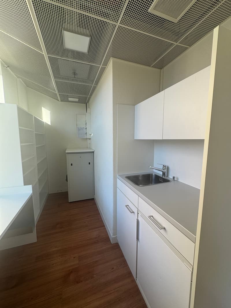 empty room with wooden floor, white cabinets, stainless steel sink, fluorescent ceiling lights