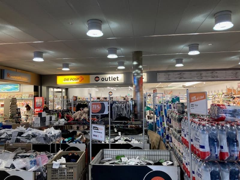 Store interior with various products on shelves, clothes on hangers, shopping carts, and a large sign indicating 'DIE POST+ outlet'.