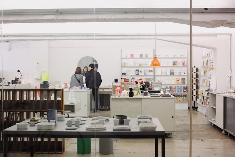 A room with a glass wall, shelves with books, a table with plates, cups, and bowls, a wooden cabinet, and a mirror.