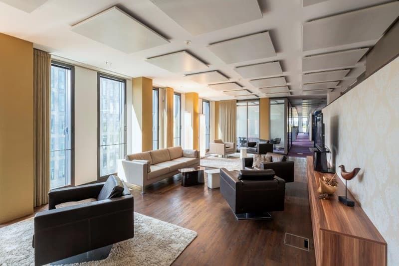 Spacious open-plan living area with large windows, hardwood floors, modern furniture including sofas and coffee tables, and a coffered ceiling design.