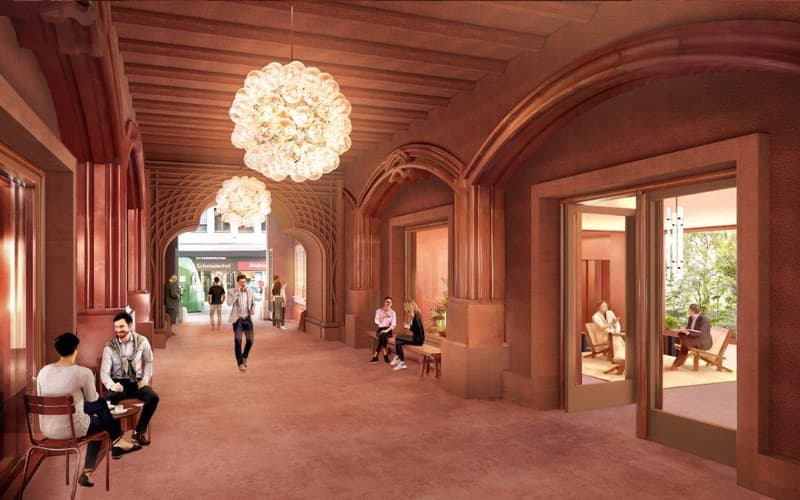 The image shows a grand, ornate interior space with high ceilings, arched doorways, and wooden beams. The space is illuminated by large, decorative chandeliers. Several people are visible, sitting and walking through the hallway. The overall atmosphere ap