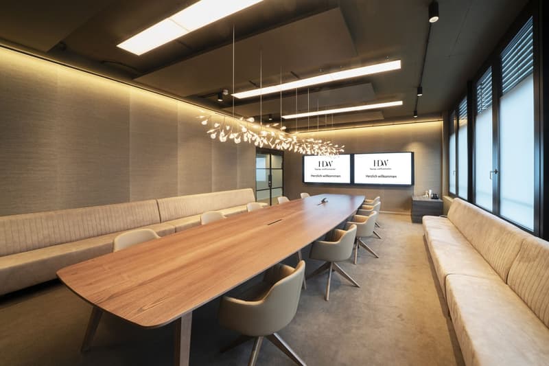 Modern meeting room with a large wooden conference table, beige upholstered benches, minimalist furniture, and modern office lighting.