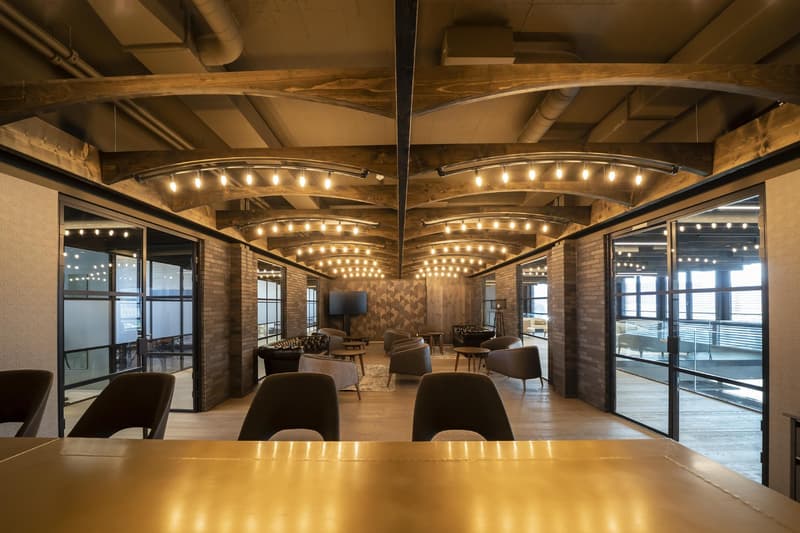 open plan with glass doors, wooden ceiling, hanging track lights, couches, tables, TV, brick walls, wooden floor