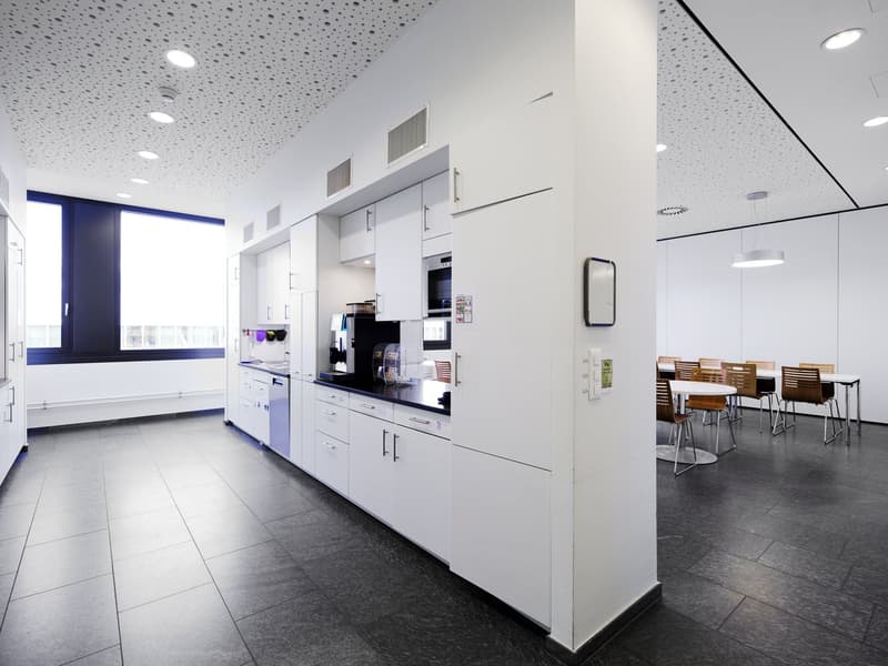 modern kitchen with white cabinets, black countertops, stainless steel appliances, tiled flooring, large window, table and chairs for dining