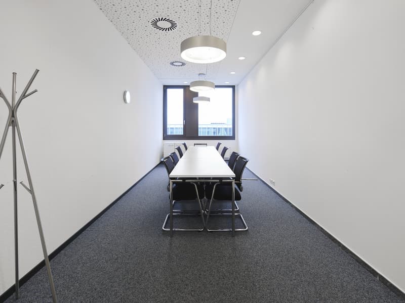 empty conference room with a long table, chairs, windows, white walls and ceiling lights