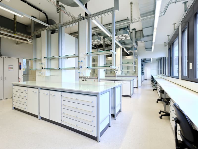Modern laboratory, white cabinets, large glass shelves, large glass windows, black swivel chairs, white countertops, glass dividers, metal railings, fluorescent lights on ceiling