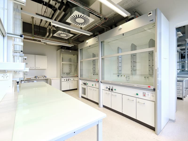 Modern laboratory with glass panels, white cabinets, white countertops, fluorescent lighting, glass shelves, and multiple control panels.
