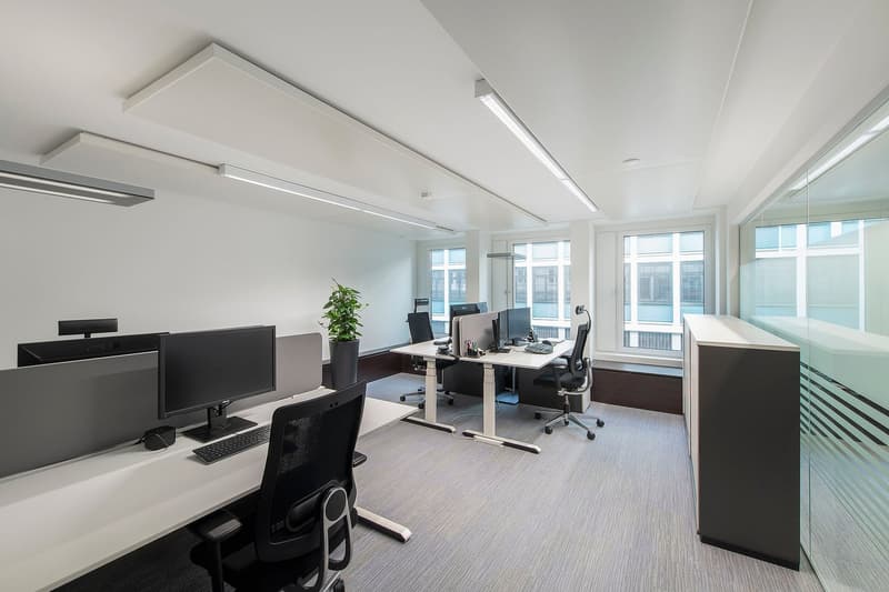 An empty office with desks, computers, chairs, and a plant.