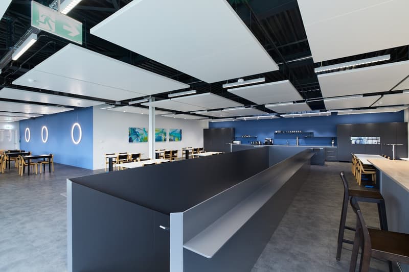 modern office space with blue walls, white ceiling panels, long counter, tables, chairs, artwork, kitchen area