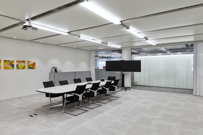 modern office meeting room, long white table, black chairs, projector, TV, artwork on wall, glass wall
