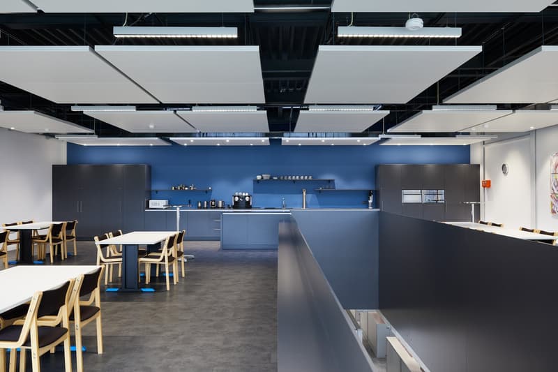 modern office space with blue walls, white ceiling panels, tables, chairs, kitchen area with appliances, cabinets, and shelves