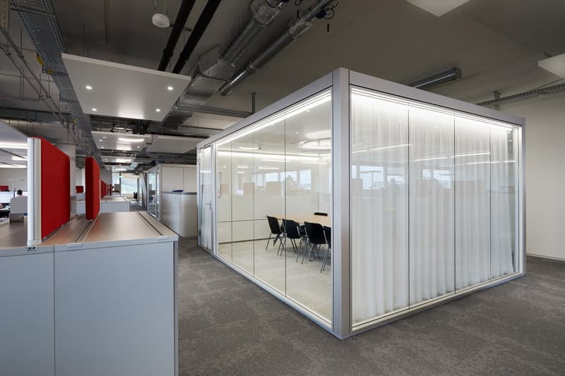 modern office space with glass walls, gray carpet, white ceiling, red partitions, meeting table, chairs